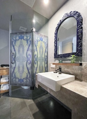 Casa de banho com cabine de duche em vidro, lavatório branco e espelho grande com moldura decorativa.