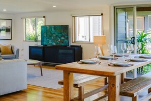 Una zona pranzo con tavolo in legno apparecchiato per quattro persone, una televisione e un quadro appeso al muro.