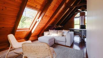 A cozy loft bedroom with a sloped ceiling, a white sofa, a wicker chair, and a desk area.