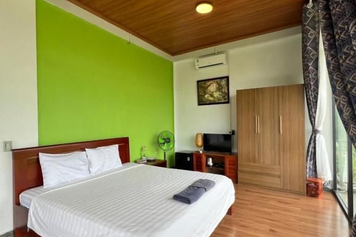 Un dormitorio con techo de madera, cama con ropa de cama blanca, pared verde y un armario.