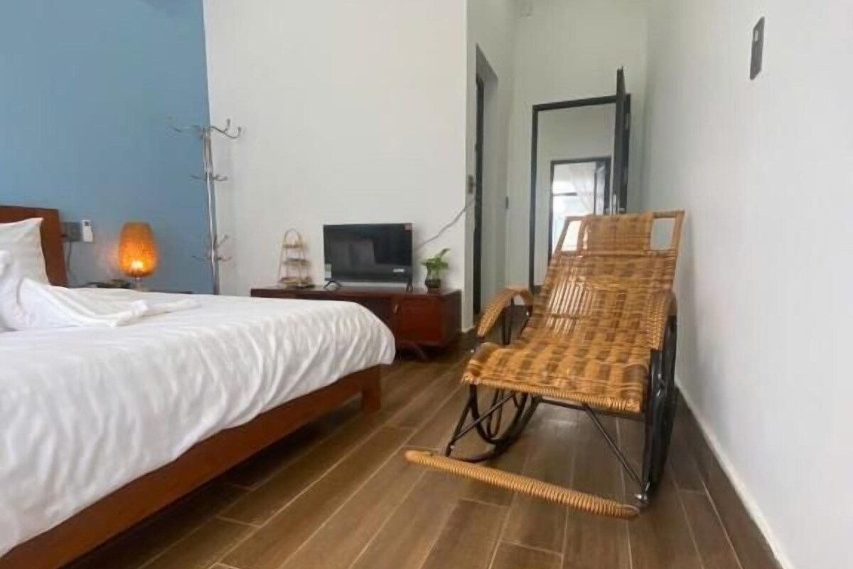 Un dormitorio con una cama, televisor, una silla de mimbre y aire acondicionado instalado en la pared.
