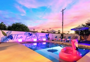 Ein Swimmingpool mit einem Flamingofloat, Liegestühlen und einem Sonnenuntergangshimmel.