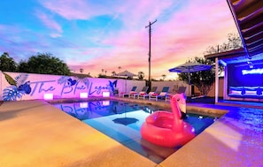 Ein Swimmingpool mit einem Flamingo-Schwimmspielzeug, Liegestühlen und einem Sonnenuntergangshimmel.