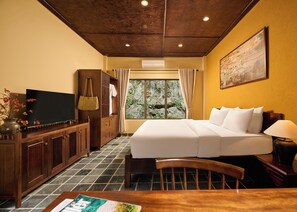 Quarto de hotel com cama, escrivaninha, televisão e janela com cortinas.