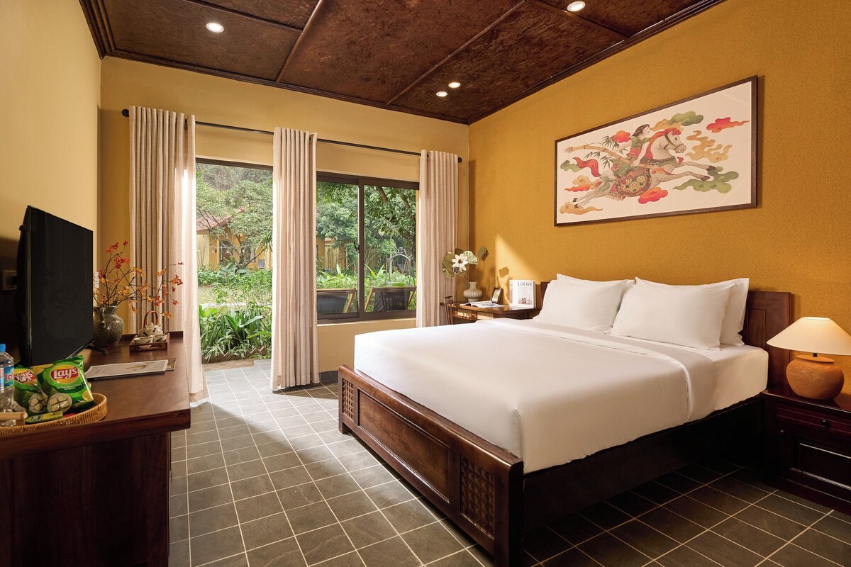 Quarto de hotel com uma cama grande, uma escrivaninha com televisão e uma janela com cortinas.