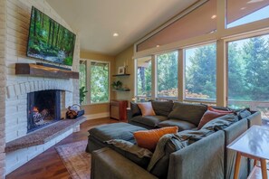A living room with a fireplace, a large TV, and a sofa with cushions. - Stylish 3BR Hillside Retreat - Hot Tub & Fire Pit (Medford)