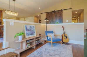 A living room with a blue armchair, a guitar, a bookshelf, and a chandelier. - Stylish 3BR Hillside Retreat - Hot Tub & Fire Pit (Medford)