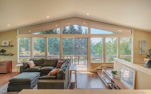 A spacious living room with a large window, a sofa, a coffee table, and a wooden bench. - Stylish 3BR Hillside Retreat - Hot Tub & Fire Pit (Medford)