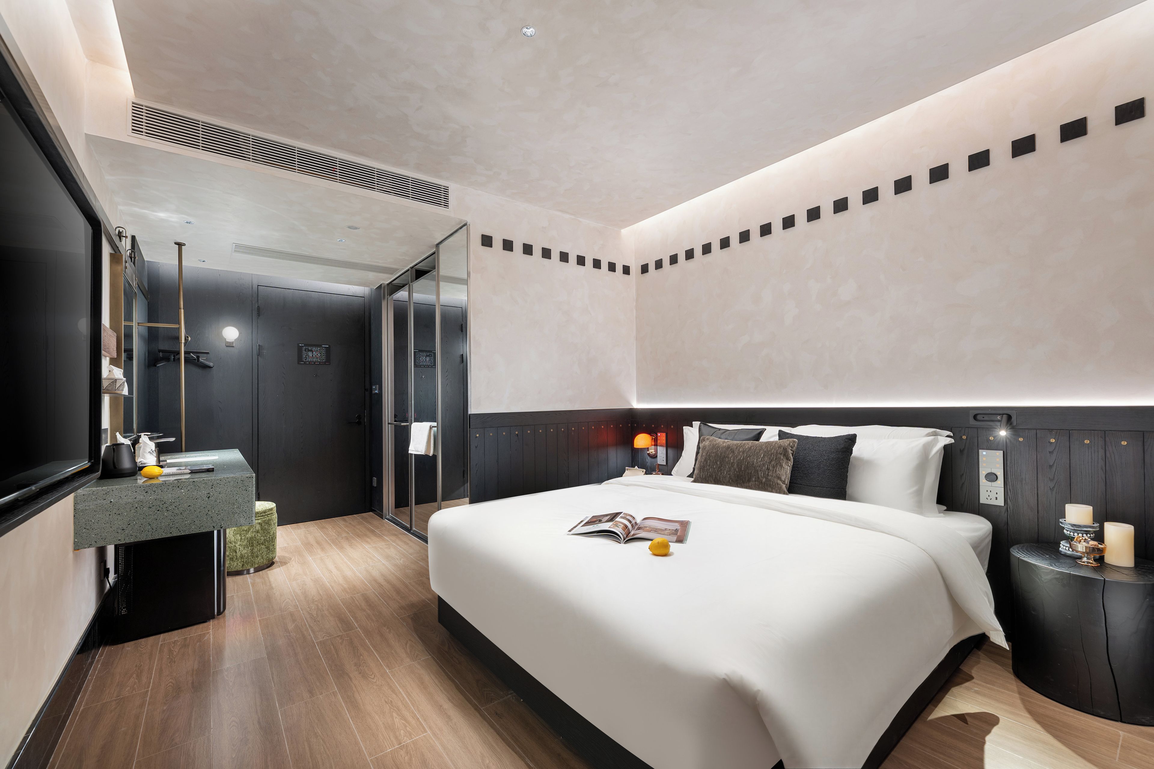 A modern hotel room with a large bed, a bedside table, a mirror, and a bathroom with a shower and toilet.