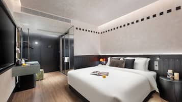 A modern hotel room with a large bed, a bedside table, a mirror, and a bathroom with a shower and toilet.