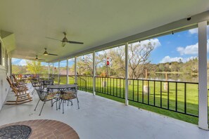 Eine überdachte Terrasse mit Gartenmöbeln, Blick auf eine Rasenfläche und einen See.