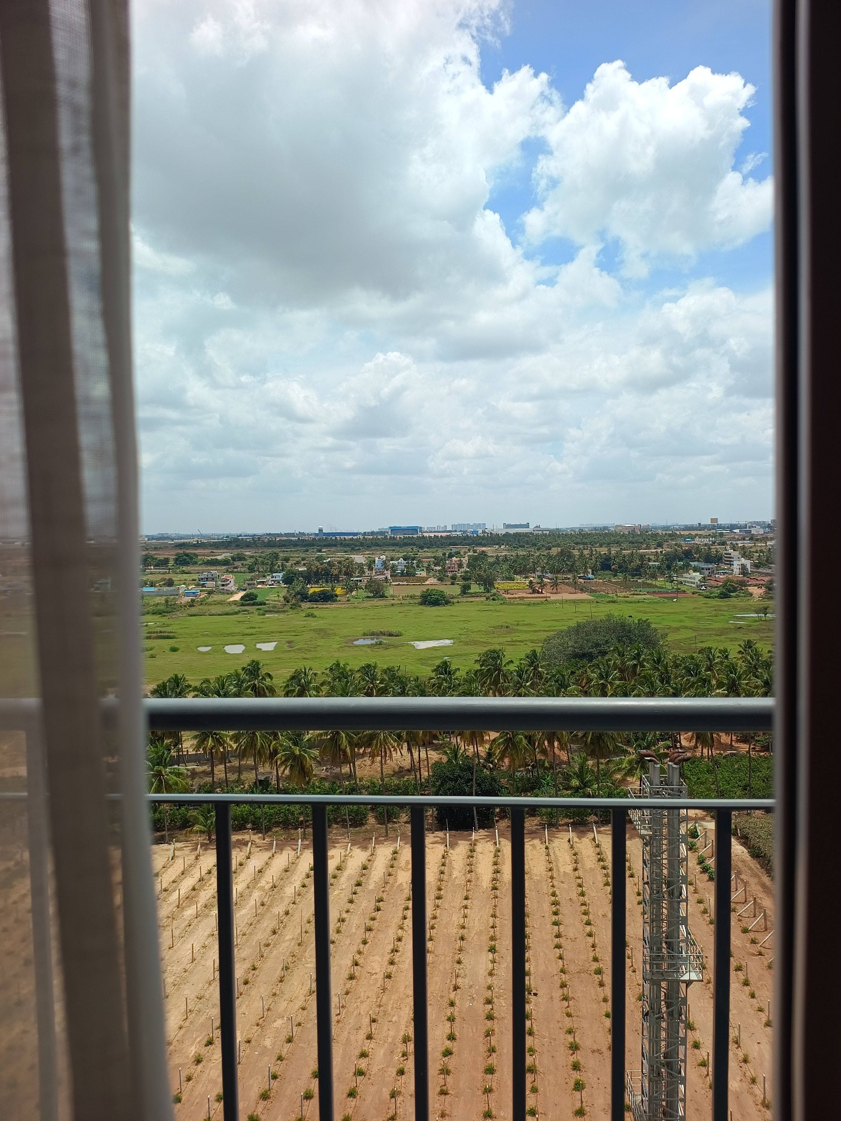 En balkon med udsigt over et grønt landskab, herunder marker og en fjern bysilhuet.