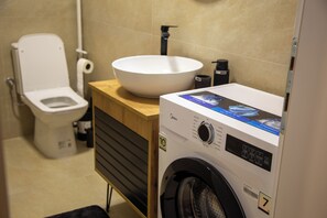 A compact bathroom with a toilet, a sink, and a front-loading washing machine. - STOUNE BRIDGE APARTMENT 24 (Skopje)