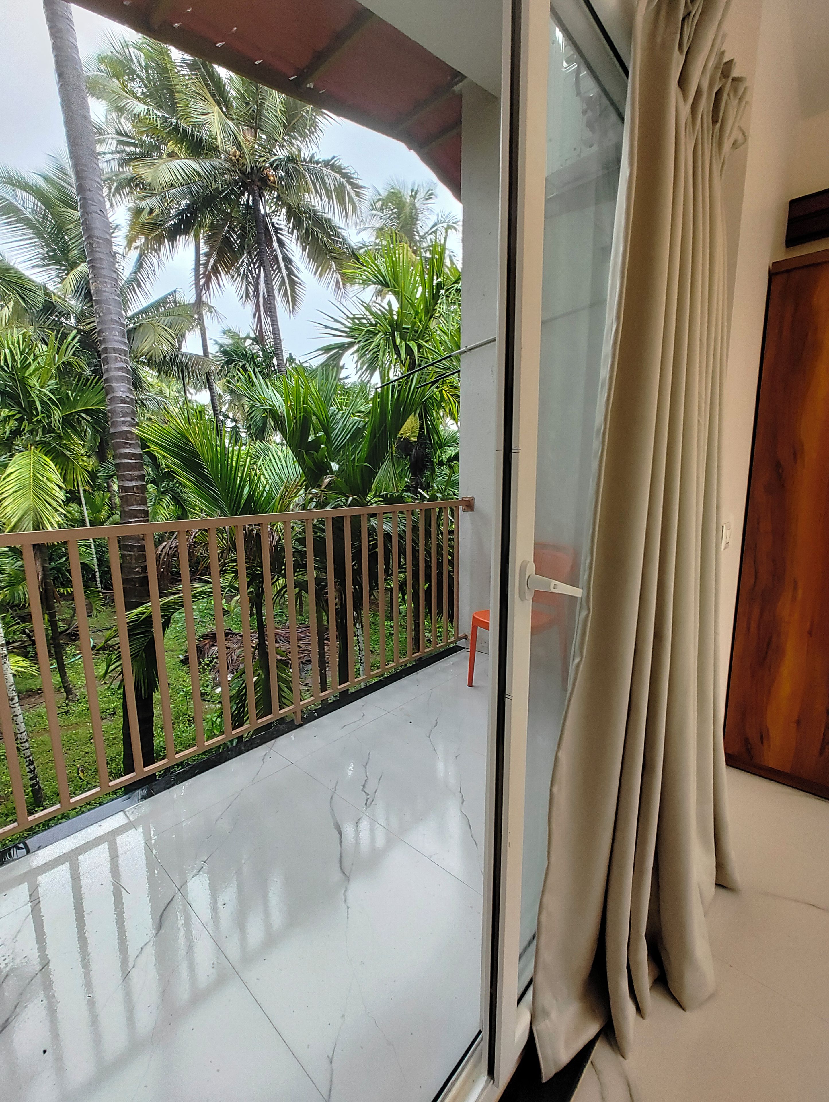 A balcony with a metal railing, a glass door with a curtain, and a view of palm trees.
