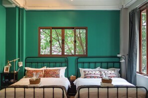 Una habitación con dos camas, un ventanal con vistas a árboles y un escritorio con lámpara.