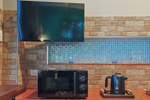 Una cocina con microondas, hervidor y televisor sobre el microondas.