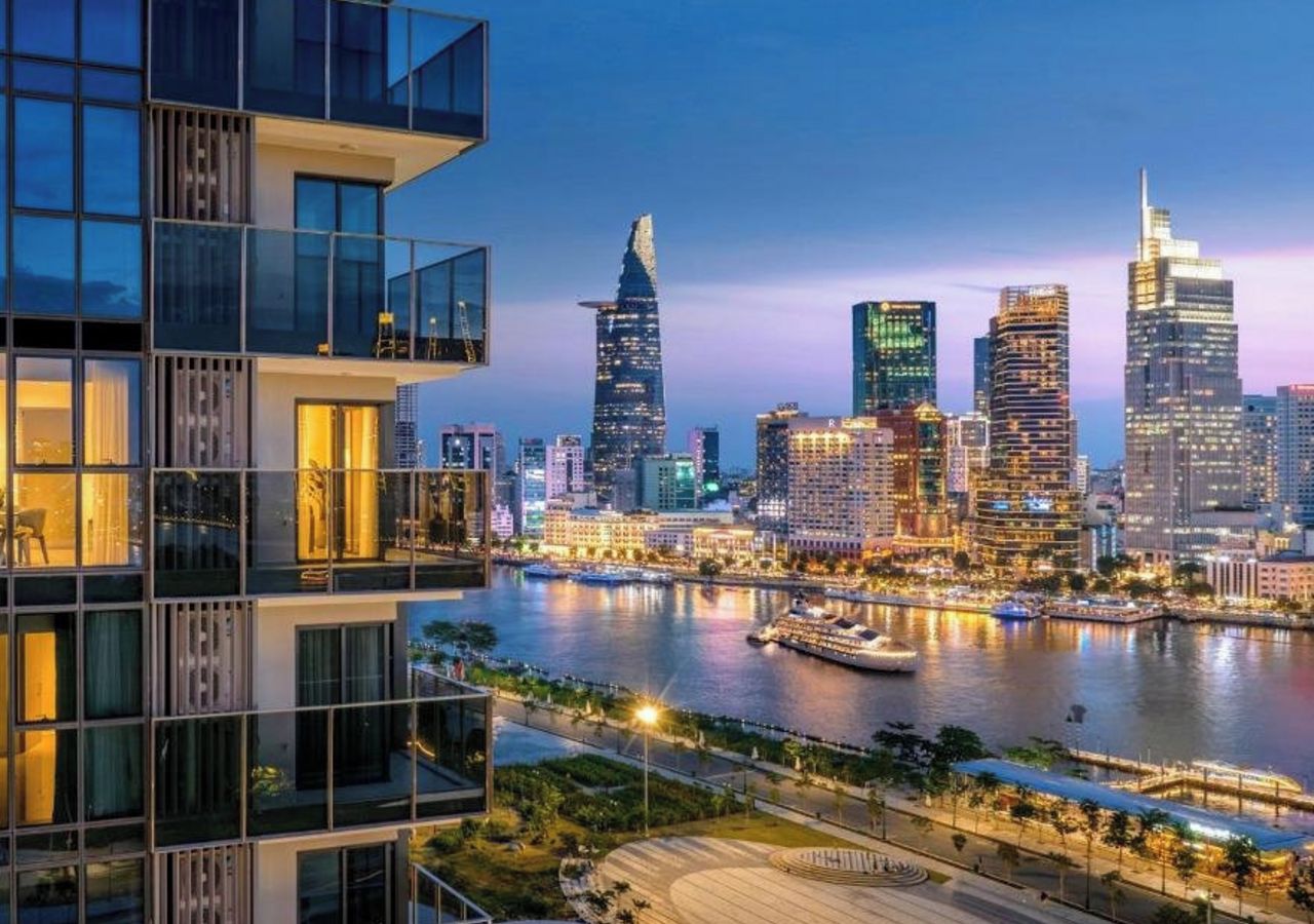 Un moderno edificio de gran altura con fachada de vidrio que ofrece vistas a un río y al horizonte urbano al atardecer.