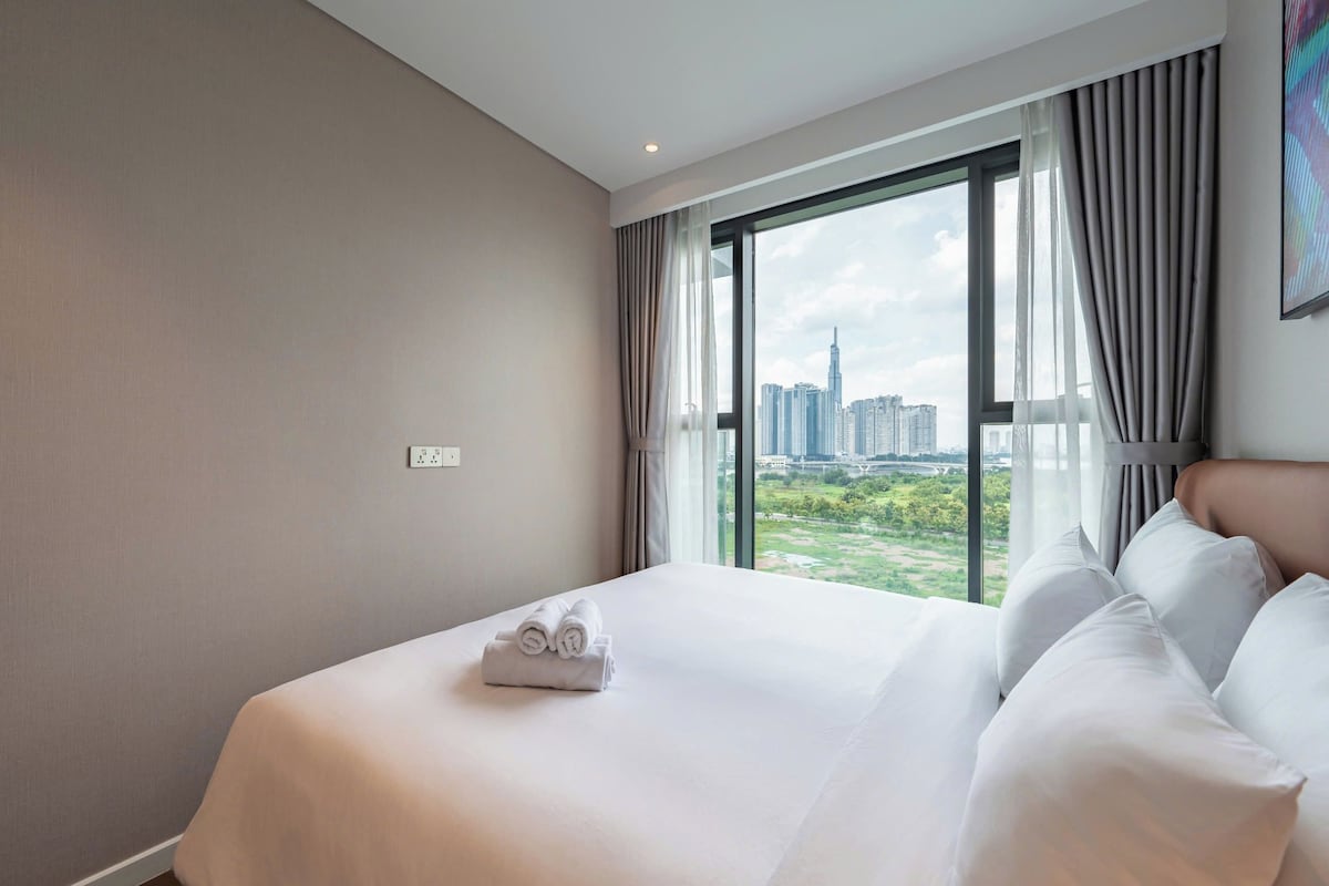 Habitación de hotel con una cama grande, vistas a un paisaje urbano y una ventana con cortinas.