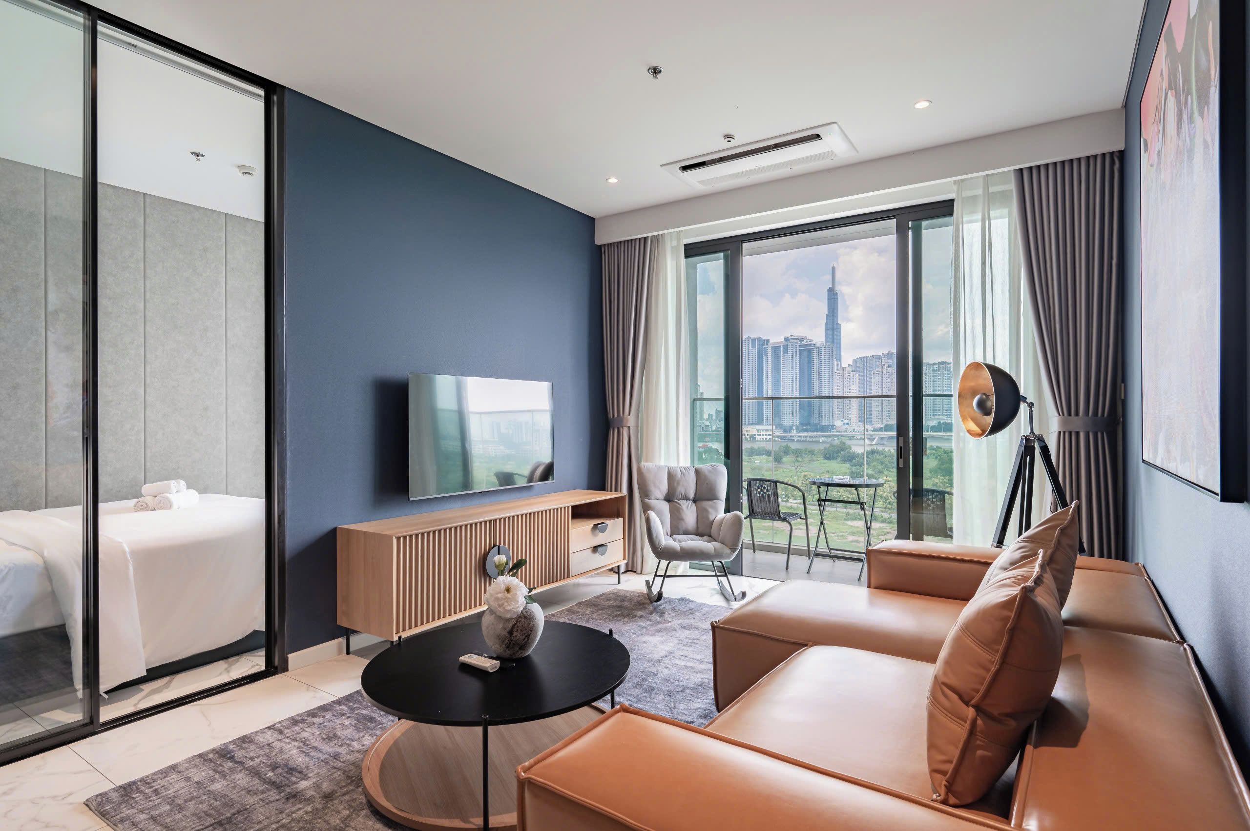 Una habitación de hotel moderna con cama, sofá, televisión, mesa de comedor y vistas a la ciudad.