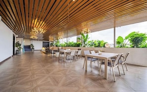 Un vaste espace intérieur doté d’un haut plafond, de lambris en bois et offrant une vue sur la verdure environnante.