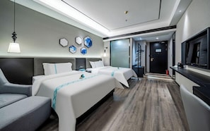 Une chambre d’hôtel avec deux lits, un canapé, une télévision et une salle de bain visible à travers une porte en verre.