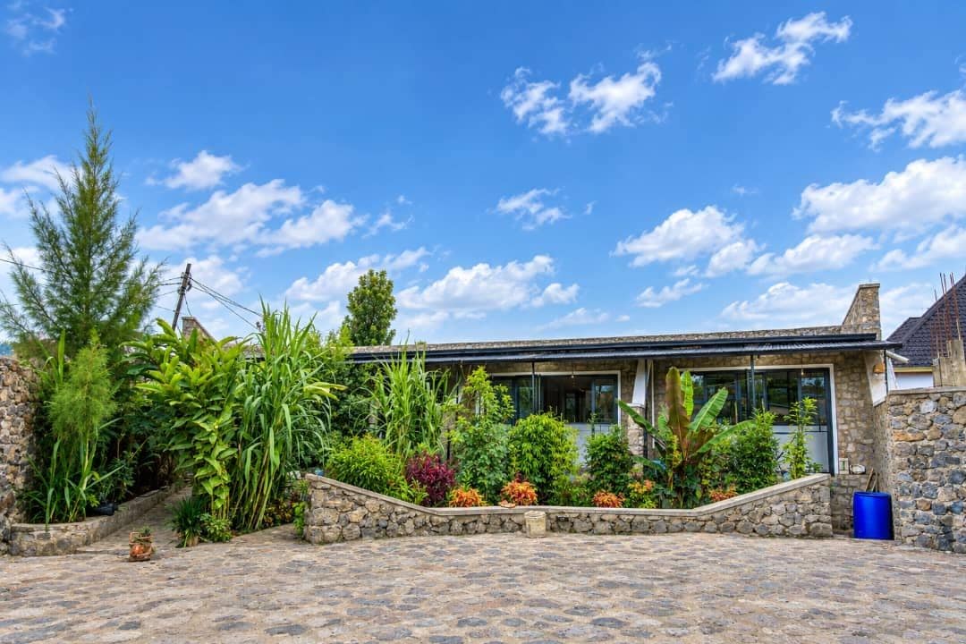 Une maison moderne avec une façade en pierre, une allée pavée et une variété de plantes et d’arbres.
