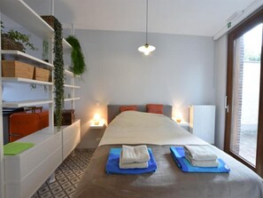 Ein Hotelzimmer mit einem Bett, Nachttischen, einer hängenden Pflanze und Blick durch ein Fenster.