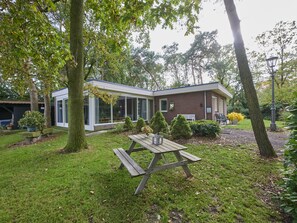 Une maison moderne dotée d’un patio, d’une table en bois et entourée de verdure.