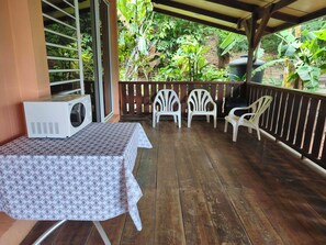 A covered outdoor area with a table and chairs, surrounded by wooden flooring and a wooden railing. - Teva's Tahiti Stay (Faaa)