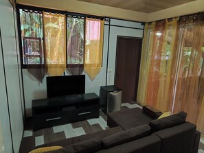 A living room with a flat-screen TV, a sofa, a coffee table, and a trash bin. - Teva's Tahiti Stay (Faaa)