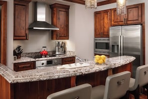 A kitchen with wooden cabinets, stainless steel appliances, a granite countertop, and a seating area with chairs. - New Year's Eve in Vail — Ritz-Carlton Club 3BR Residence (Vail)