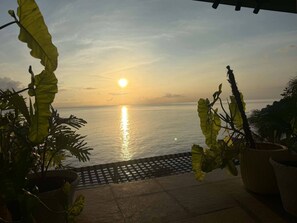 Vista do mar ao pôr do sol, com plantas em vasos ao primeiro plano.