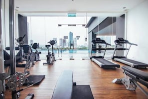 Ein Fitnessstudio mit Cardiogeräten, Krafttrainingsgeräten und Blick auf eine Stadtkulisse durch große Fenster.