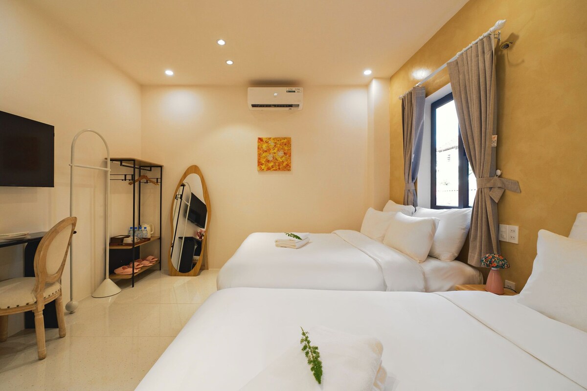 A hotel room with two beds, a desk, a chair, a TV, and an air conditioning unit.