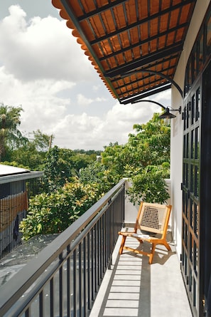 A balcony with a wooden chair, a tiled floor, and a view of greenery.