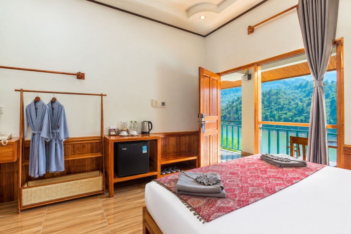 Een hotelkamer met een bed, een televisie, een houten bureau, een plank met toiletartikelen, en een balkon met uitzicht op de omgeving.