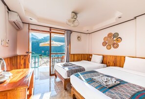 Een hotelkamer met twee bedden, een houten hoofdbord, een balkon met uitzicht en een tafel met waterkoker.
