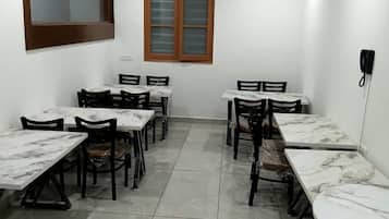 Un salón de conferencias con mesas de mármol, sillas negras, un ventilador de techo y un teléfono en la pared.