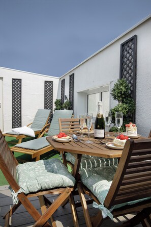 Une terrasse extérieure avec des meubles en bois, une table dressée pour un repas et une bouteille de champagne.