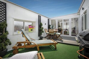 A patio with a sun lounger, wooden table, chairs, and a grill. - Granada Apartments Queen's Mansions flat 10 Queen Suite 3rd floor front sea view (Blackpool FY2 9HP)