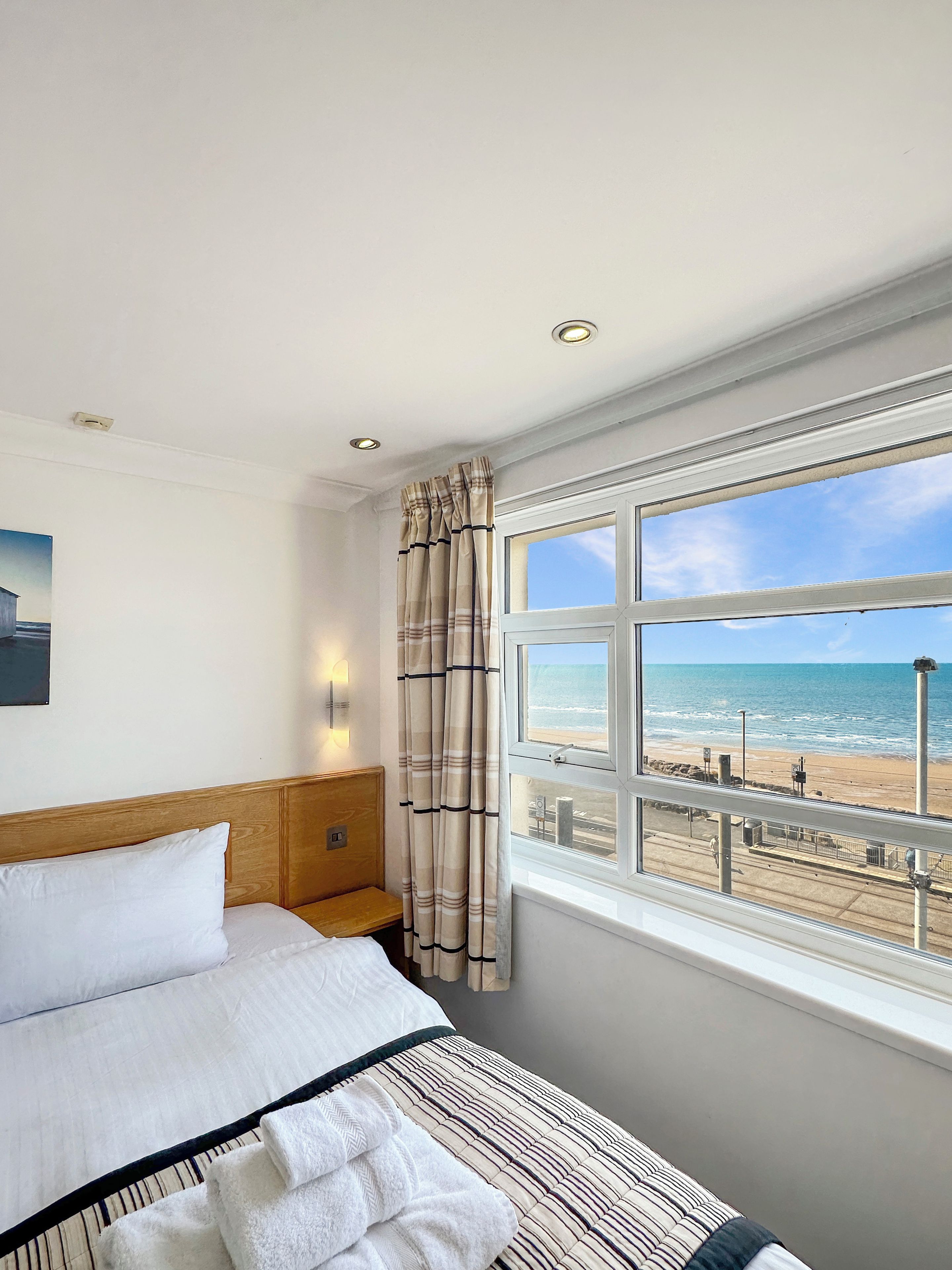 Quarto de hotel com cama, vista para a praia e janela com cortinas.
