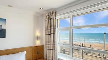 Quarto de hotel com cama, vista para a praia e janela com cortinas.