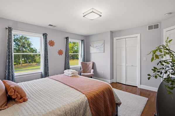 Quarto com cama, cadeira, janela com cortinas, porta e planta.
