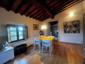 A dining area with a wooden table and chairs, a window with a view, and a painting on the wall. - New Listing (Toscana)