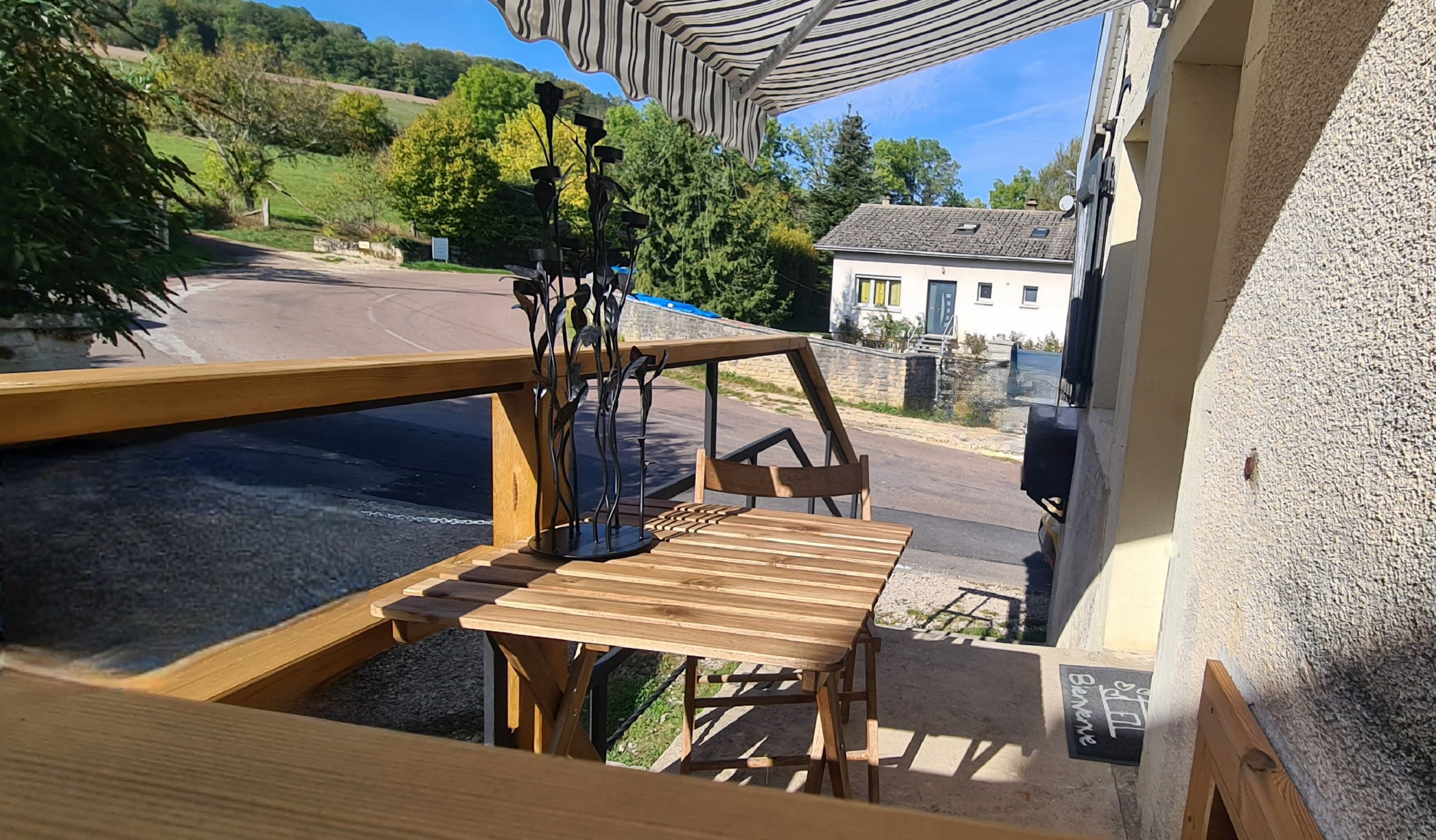 A wooden deck with a table and chairs, overlooking a road and a building.