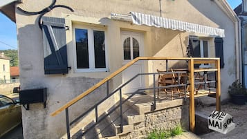 A building with a staircase leading to a wooden deck area, a sign reading 'LAW PETE MAISON,' and a window with a shutter.