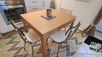 A small dining area with a wooden table, two chairs, a cup, and a doormat with 'LAW PETE MAISON' text.