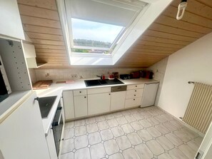 Kompakti keittiö, jossa on kattovalokuvio, valkoiset kaapit, musta työtaso ja kuusikulmaisista laatoista tehty lattia.