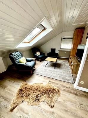 Une pièce de style loft avec un plafond en pente, un fauteuil en cuir noir, une table basse en bois, un tapis en fourrure et un téléviseur.