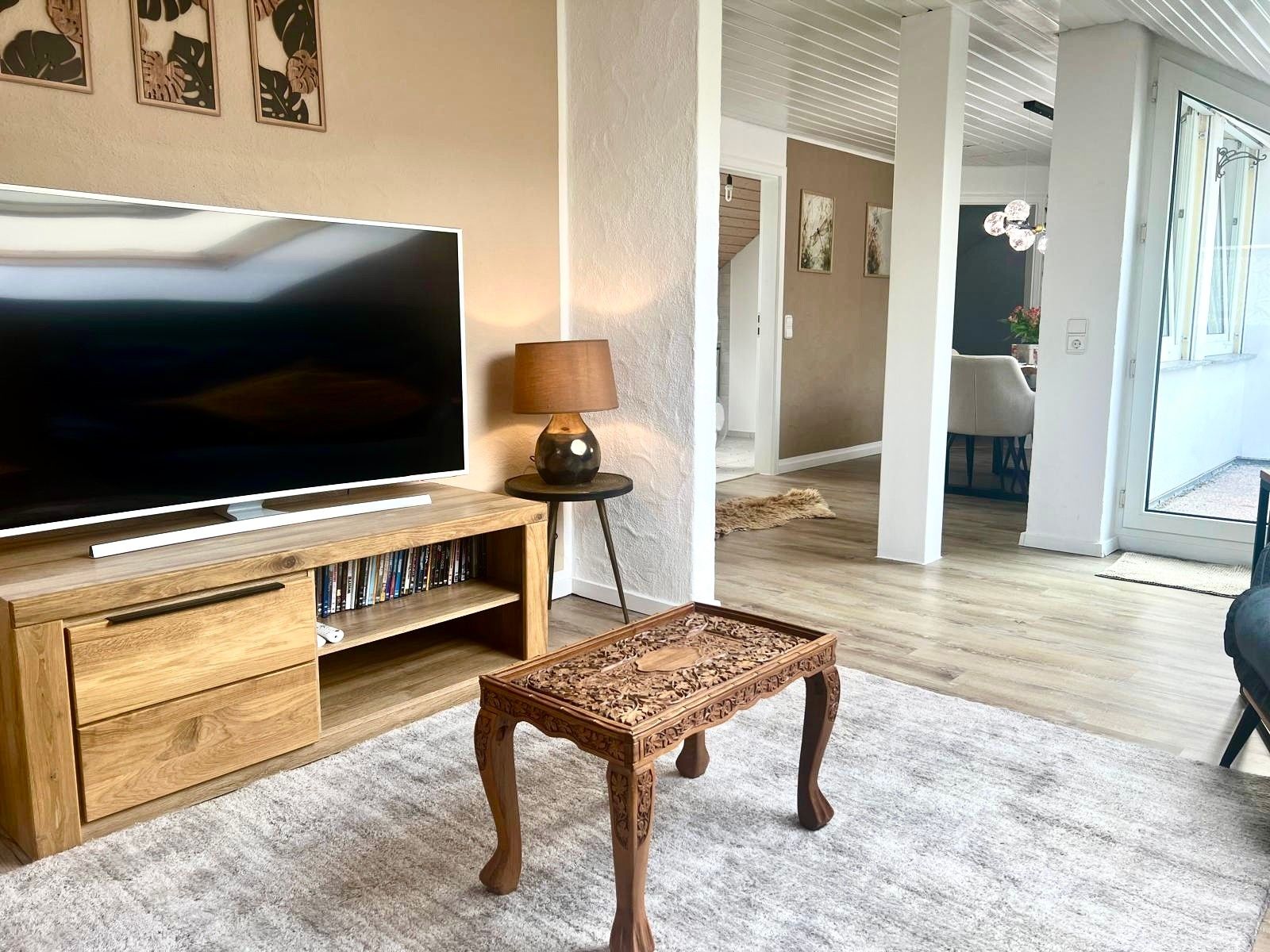 Un salon équipé d’un téléviseur à écran plat, d’un meuble de rangement en bois, d’une petite table et d’une lampe.